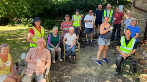 Management Team, Punch Bowl Inn, Burton in Lonsdale A mixed gender group of people, some in high-visibility jackets stand and sit in a sunny garden.