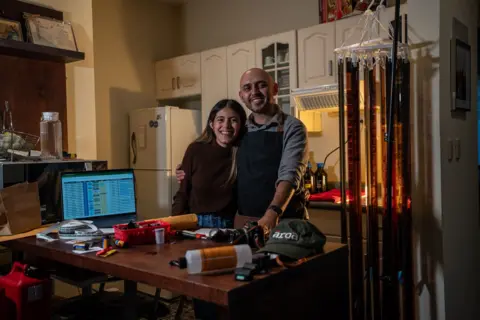 Fritz Pinnow Fabriccio Díaz and Lucía Ramírez embrace in their kitchen where they develop the entire film for the Arca Film Lab. On the desk in front of them, bottles of chemicals can be seen and rolls of film are drying. 