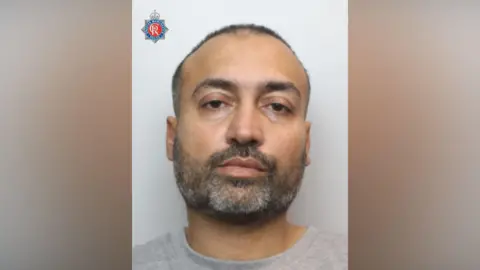 The mugshot of a man with a greying beard and close-cropped hair.