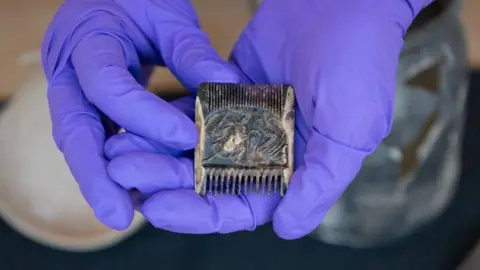 HES A close-up of a comb held in gloved hands 