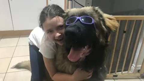 Supplied A young girl hugging a large dog with his tongue out and sunglasses on