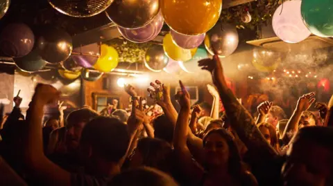 Mike Baxter A large group of people dancing beneath disco balls and balloons at Gonzos.