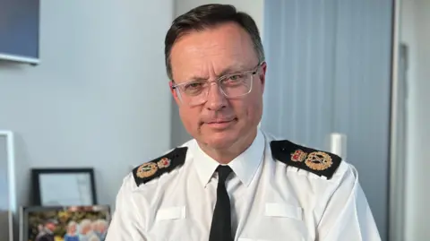 Robin Smith wearing his police uniform sitting at his desk in a police office.