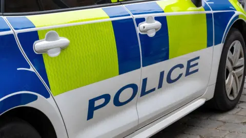 Getty Images A close-up picture of a police car with the word police in blue capital letters written along the side. There are blue and yellow police markings also on the side of the car.