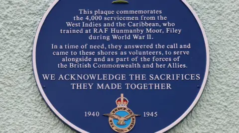 RAF A blue plaque on a wall commemorating the service of 4,000 men from the Caribbean who served in the RAF during World War II and trained initially at RAF Hunmanby Moor near Filey