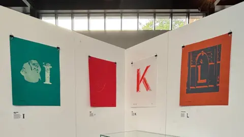 Supplied Four coloured prints pinned to tall white boards on display. 