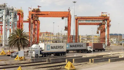 AFP via Getty Images Trucks loading and offloading containers at a harbour terminal in Cape Town.