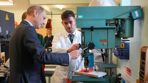 Aaron McCracken The Duke of Edinburgh, Prince Edward, helps put a Joint Award Initiative logo on a plastic orange bowl. He is in a Technology and Design classroom and is joined by the teacher of the class. 