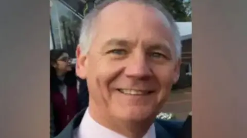 Cumbria Police Paul Taylor. He is wearing a suit and tie and is smiling at the camera. He has short grey hair and blue eyes.