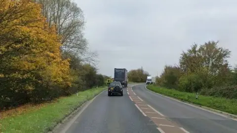 Two single carriageways of the A47 on a bend, with a lorry and a car travelling in one direction and a white lorry travelling in the other.