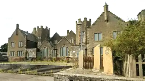a derelict old school building with turrets and boarded-up windows