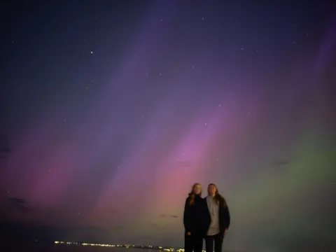 Catherine Heymans The Northern Lights from Portobello Beach in Scotland. There are green and purple stripes across the sky with Catherine Heymans and her teenage daughter in the foreground. 