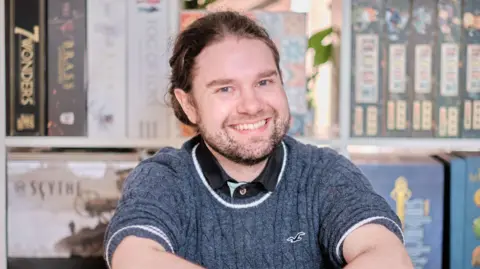 HANDOUT Kari, who has long brown hair tied back and is wearing a grey knitted jumper, smiles 