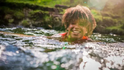 Cheerful young woman splashing water while enjoying swim with friends in sea on sunny day