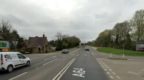 Google A64 crossroads between Scarborough/Malton and York, close to Crambeck Village. A white van in the foreground with other cars driving away from and towards the camera. A brown sign for Castle Howard to the left.