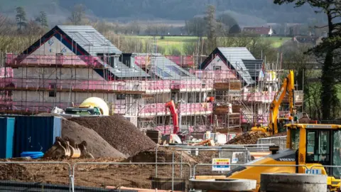 A stock image of a housing development being built, with scaffolding over a property and heavy machinery in the foreground