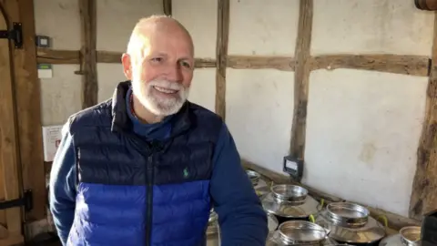 BBC Charles Martell has a grey beard and is wearing a blue jacket in front of some barrels 