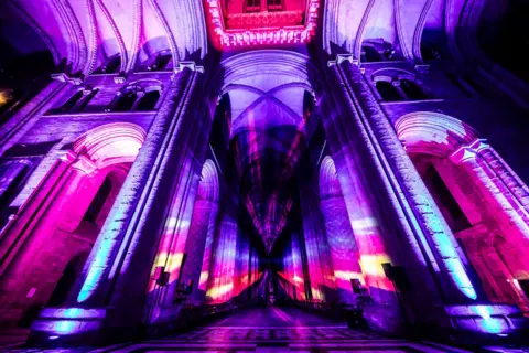 Peter Walker Inside the cathedral is lit up in yellow, purple, blue and pink. 
