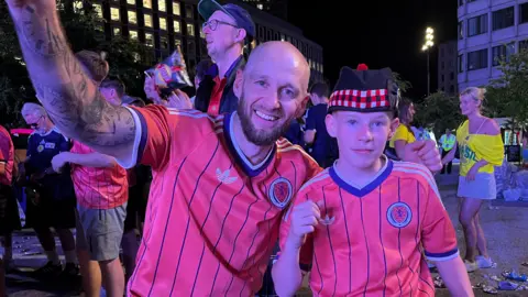 Chris Goodman celebrates with his son Jack. They both have their arms raised and are wearing Scotland away strips.