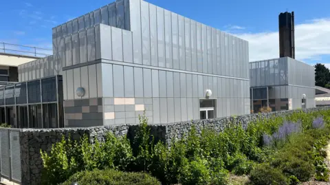 BBC A large grey building with a chimney at the back. 