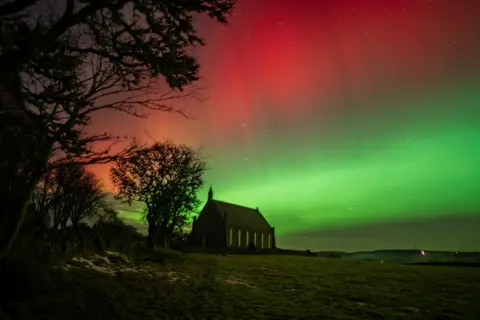 David/BBC Weather Watchers A red and green display of the aurora behind a church in Bonar Bridge.