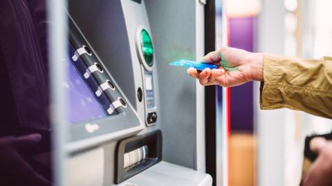 Female hand inserting bank card into automatic cash machine