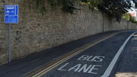 Bus Lane on Lanark Road in Edinburgh. There is a blue sign stating the times cars are not allowed to use the bus lane.