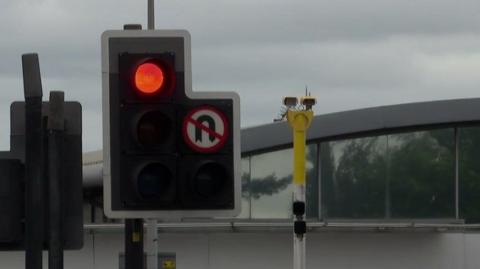 A red light on a set of traffic lights, with yellow speed cameras placed next to them