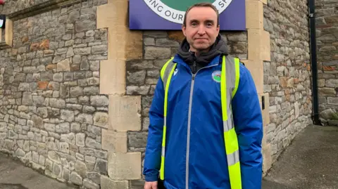 Chris Barratt, the principal of Summerhill Academy in St George, standing in front of the school. He is wearing a high-vis jacket and is smiling at the camera