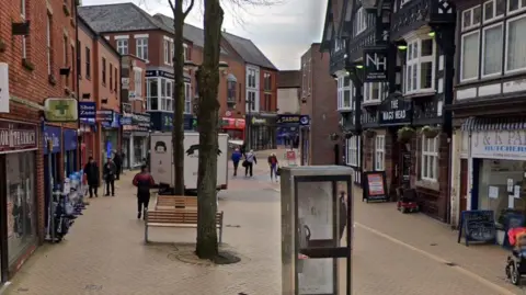 A view of Low Street which shows a pedestrianised high street. There is a phone box in the centre and a range of shops along with a pub