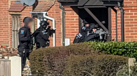 Tabi C S Nicholls Four armed police officers at the a doorway of a property.