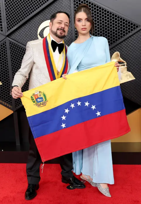 Getty Images Raniero Palm sostiene una bandera venezolana mientras posa en la alfombra roja con Mariana Salas