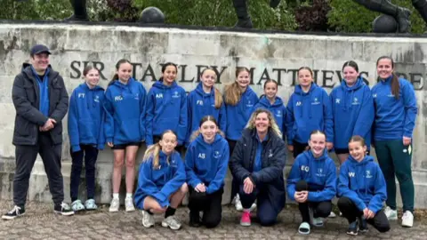 The Bournemouth School for Girls under-12s team standing in blue hoodies in front of a statue of Sir Stanley Matthews