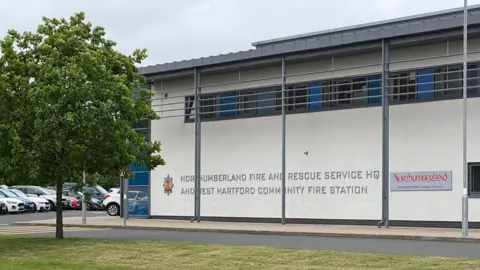 Mark Denten/BBC Exterior of Northumberland Fire and Rescue Service's headquarters at West Hartford Community Fire Station in Cramlington. The organisation's logo is on the side of the building, which is white with a grey roof.
