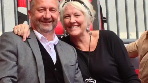 Jen Jackson has her arm around her husband Phil as they smile at the camera. 