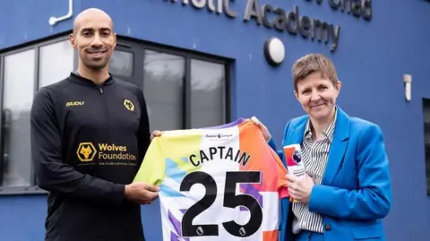 Premier League Ex-Wolves captain Karl Henry with Louisa Craig after surprising her with the award. They are standing outside the school and holding a special shirt.