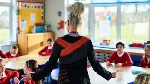 Primary school teacher standing with arms out, preparing children for class.