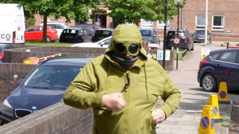 Man in green hoodie with attached goggles covering his eyes and a scarf over his face