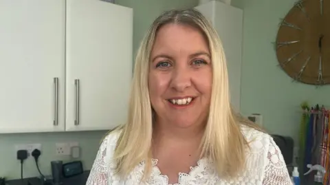 A woman with blonde hair wearing white lace top smiling at the camera.