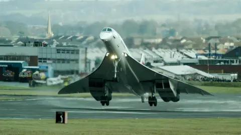 Concorde takes off from a runway with its nose drooped down.