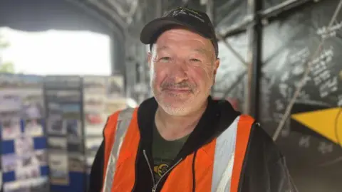 Josh Mortimer in a cap and orange hi-vis smiling into the camera