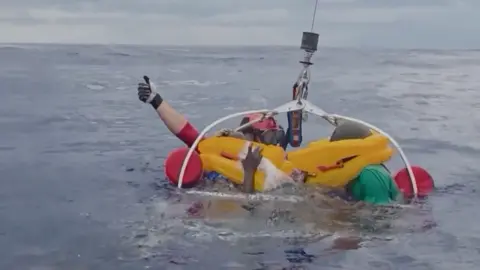 Two people in life jackets are hoisted to safety in the waters.