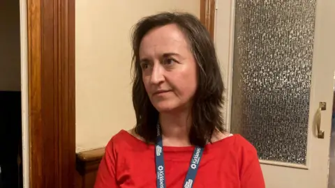 A woman with dark, long hair and wearing a red top 