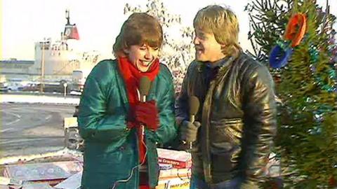 Keith Chegwin and Maggie Philbin looking very cold, standing in a car park in front of a Christmas tree.