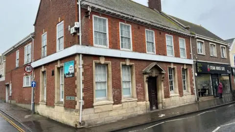 Andrew Turner/BBC The former Barclays on Gorleston High Street is a 1920s building with red brickwork and stone mullions and foundation work. It has a Georgian-style entrance and a white fascia which once bore the Barclays sign. Above that white band is a first floor of sash windows, leading to a slate roof