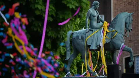 The green statue of Godiva in Coventry, with colourful paper streamers draped over