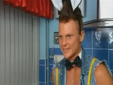 Channel 4 Tomasz appearing on Come Dine With Me in 2011. He is in his kitchen with bunny ears, a bow tie and a denim gilet. 