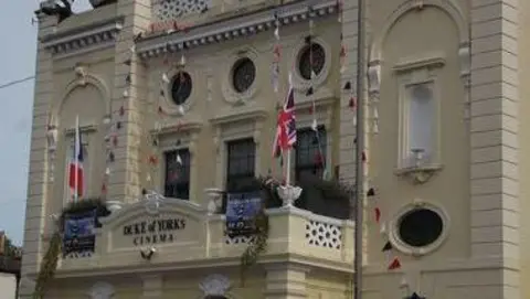 The Duke of York's cinema in Brighton, East Sussex with a balcony to the first floor, and flags at each side and planing around the edge