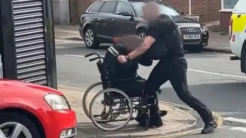 A policeman appears to hit a man in a wheelchair.