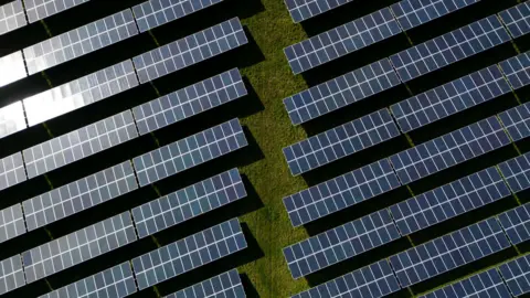 An aerial view shows rows of black photovoltaic (PV) solar panels.